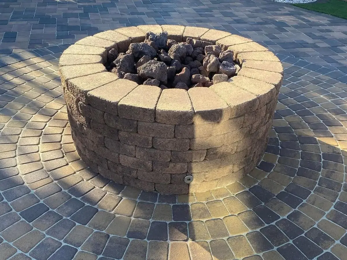 Round stacked block firepit set into a circular paver patio with lava rock